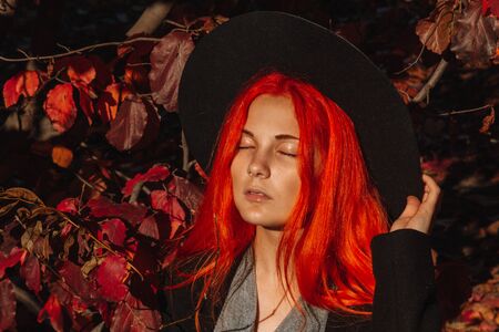 Sexy beautiful redhead girl with long hair. Perfect woman portrait on a background of yellow foliage. Gorgeous hair and deep blue eyes. Natural beauty, clean skin, face and hair careの写真素材
