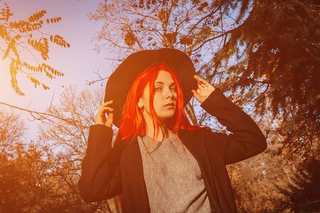 Sexy beautiful redhead girl with long, strong and thick hair in a black hat and coat. Perfect woman portrait. Gorgeous deep blue eyes. Natural beauty, clean skin, face and hair careの写真素材