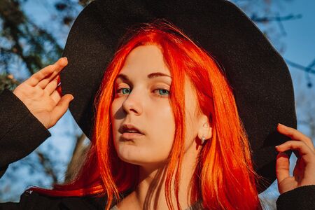 Sexy beautiful redhead girl with long, strong and thick hair in a black hat and coat. Perfect woman portrait. Gorgeous deep blue eyes. Natural beauty, clean skin, face and hair careの写真素材