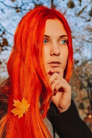 Sexy beautiful redhead girl with long, strong and thick hair. Perfect woman portrait on a background of autumn foliage. Gorgeous deep blue eyes. Natural beauty, clean skin, face and hair careの写真素材