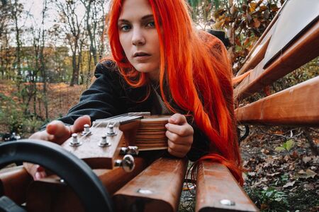 Red-haired girl with long hair plays on the ukulele in the park. School, music education concept, student learns to play the string instrument. Hands of a musician, classical, melody, creativityの写真素材