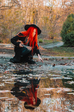 Red-haired girl with long hair plays on the ukulele in the park. School, music education concept,...