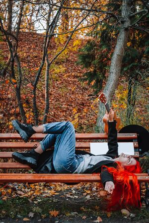 Red-haired girl with long hair plays on the ukulele in the park. School, music education concept, student learns to play the string instrument. Hands of a musician, classical, melody, creativityの写真素材