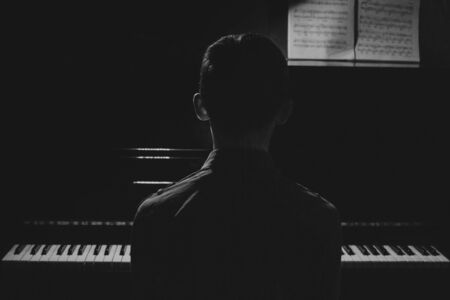 Silhouette of a young man sitting at the piano. The boy emotionally plays the keyboard in a music school. student learns to play. hands of a pianist. black and white photographyの写真素材