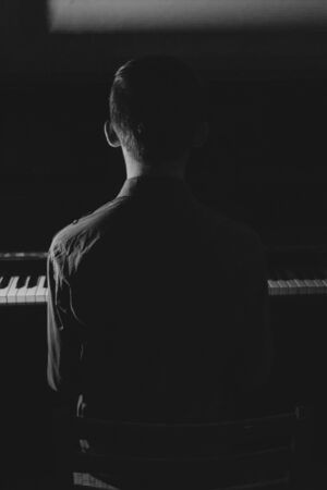 Silhouette of a young man sitting at the piano. The boy emotionally plays the keyboard in a music school. student learns to play. hands of a pianist. black and white photography. verticalの写真素材