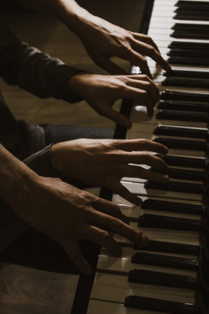 playing four male hands on the piano. palms lie on the keys and play the keyboard instrument in a music school. student learns to play. hands of a pianist. black dark backgroundの写真素材