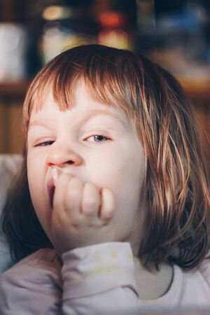 A one-year-old smiling girl sits at a children's table in a high chair and eats with a spoon from a bowl. Colored background. Healthy eating for kids. Baby foodの写真素材