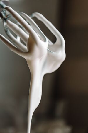 Baking concept. Whipped cream of egg whites for perfect peaks in a glass bowl, with a mixer on a marble white table. Meringue cookie recipeの写真素材