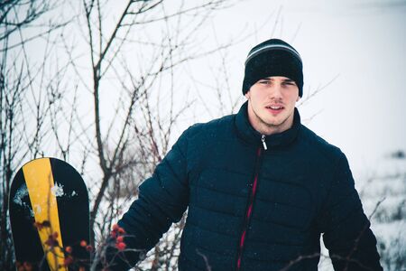Happy young man with snowboard enjoying sunny weather in snowy mountains. Winter sport and recreation, leasure outdoor activitiesの写真素材