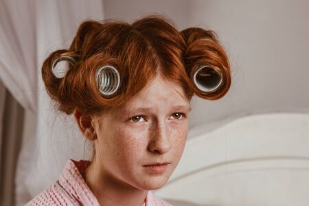 Displeased red-haired girl holds her arms crossed near the face. She looks with a sullen expression, being unhappy as she was curled on hair curlers. Does not want to have a curly hairstyle, posingの写真素材