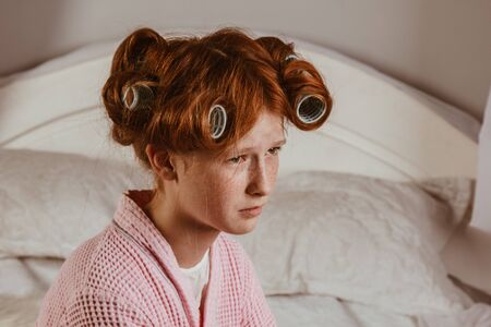 Displeased red-haired girl holds her arms crossed near the face. She looks with a sullen expression, being unhappy as she was curled on hair curlers. Does not want to have a curly hairstyle, posingの写真素材
