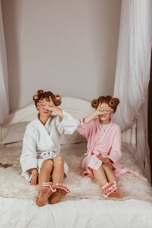 Mom and daughter at home make a mask of cucumber. Drawn eyes on the hands. Beauty Salon Concept. Beautiful face. Woman and happy baby. Girls with curlersの写真素材