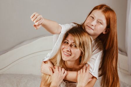 Happy mother's day. Mom and her daughter are playing girl, smiling and hugging in bed. Family holidays and togethernessの写真素材