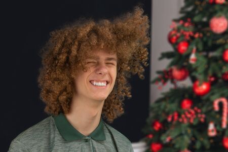Celebration, people and holidays concept - happy curly guy while Christmas or New Year party on the background of a beautiful Christmas treeの写真素材