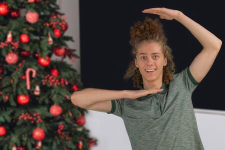 Celebration, people and holidays concept - happy curly guy while Christmas or New Year party on the background of a beautiful Christmas treeの写真素材