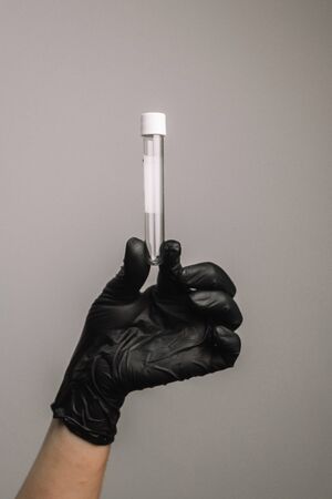 Empty test tube in a glass flask in the hands of a scientist or cosmetologist. Black gloves on a gray background. Experiment, analyzes, girl from the backの写真素材