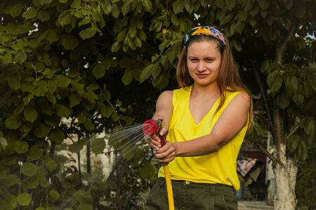 young pretty girl having fun in the garden watering plants with a hose. Smiling while taking a favorite hobbyの写真素材