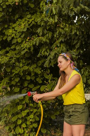 Beautiful young smiling woman watering plants in her garden with a garden hose. hobby conceptの写真素材