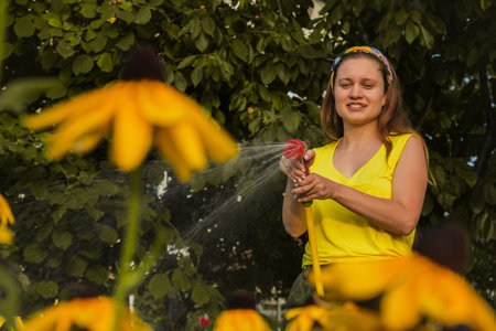 young pretty girl having fun in the garden watering plants with a hose. Smiling while taking a...