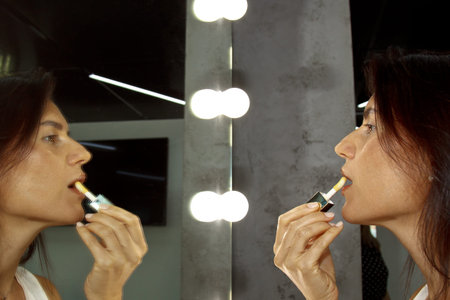 Portrait of a beautiful woman. The girl paints her lips with a colorless gloss. The model looks in...