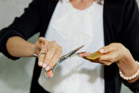 Young girl hairdresser holds scissors on outstretched hand to the viewer, standing on a gray...