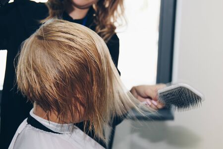 Close up of hairdresser hands drying human hair with equipment. Woman holding a comb. close-up. Macro photoの写真素材