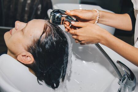 Gorgeous cheerful elderly woman enjoys a head massage while washing her hair by a professional hairdresser. Beauty care, hairstyle, fashion, lifestyle glamor concept. Drops of water and shampoo foamの写真素材