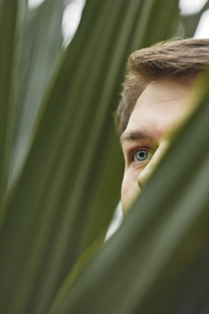 Portrait of a young man in green leaves. A nice guy is standing against a wall of green plants. A...