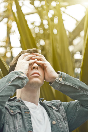 Handsome man in depression. Not shaved hipster in a botanical garden, holding on to his head....