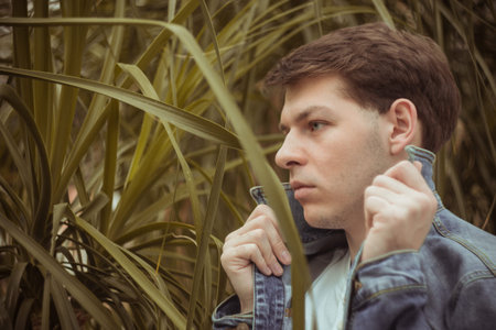 Portrait of a young man in green leaves. A nice guy is standing against a wall of green plants. A...