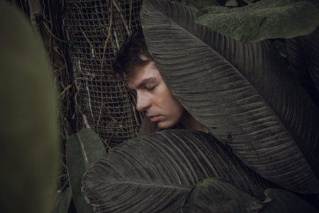 Portrait of a young man in green leaves. A nice guy is standing against a wall of green plants. A...