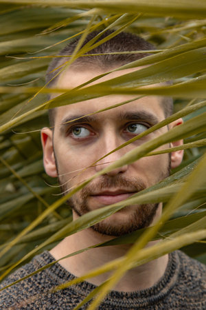 Conceptual portrait of a man in a lot of leaves. Handsome guy model posing among the thickets....
