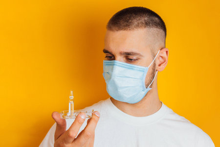 Portrait of a young guy in a respirator on a yellow background. Holding an ampoule with a...