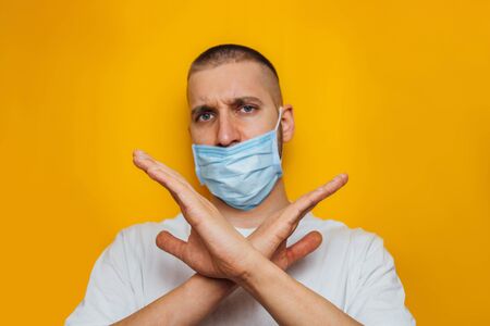 The masked guy looks at the camera and shows a stop gesture. Against quarantine. Sit at home. Cold, flu, virus, epidemic conceptの写真素材