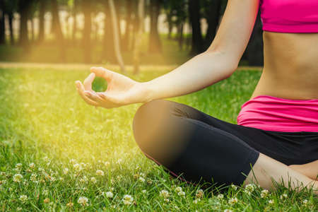 European girl in a light tracksuit doing yoga in the park in the afternoon in the summer. Gymnastics in nature. Thin woman outdoor.の写真素材