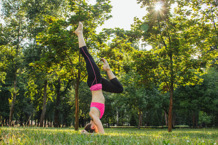 European girl in a light tracksuit doing yoga in the park in the afternoon in the summer. Gymnastics...
