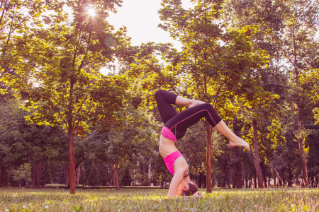 European girl in a light tracksuit doing yoga in the park in the afternoon in the summer. Gymnastics...