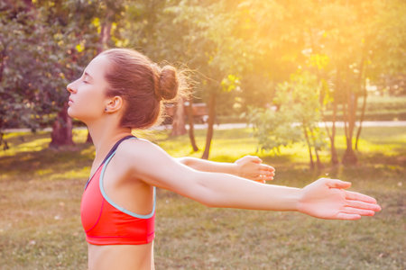 European girl in a light tracksuit doing yoga in the park in the afternoon in the summer. Gymnastics in nature. Thin woman outdoor.の写真素材