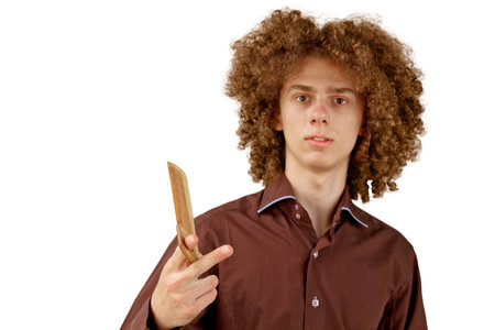 A long-haired curly-haired guy in a brown shirt on a white background uses a wooden comb. Emotions before a haircut in a hairdresser.の写真素材