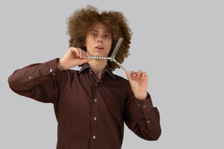 A long-haired curly-haired guy in a brown shirt on a gray background uses a metal comb. Emotions...