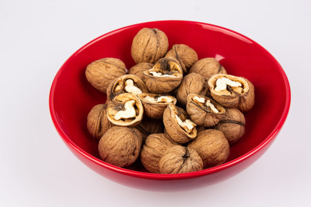 Walnuts in a red bowl isolated on white background. Nuclei in the shape of a heart. Healthy...