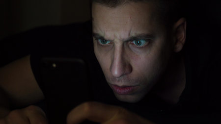 The guy in the dark room looks at the phone. Is surprised after winning the game