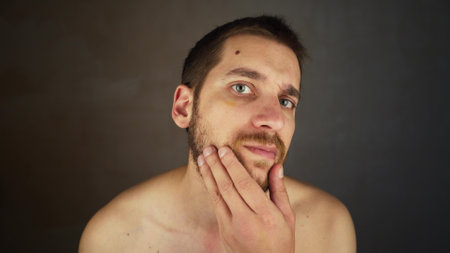 The guy is getting ready to shave. Close-up portrait of a young smiling handsome caucasian man standing in the bathroom. Healthy bearded man looks at the cameraの写真素材