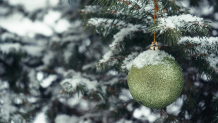 Snow is falling on the decorated spruce tree branches at Christmas. The outdoor landscape design with a festive blue decorative ball in close-up. A snowy scene in December, waiting for the New Yearの写真素材
