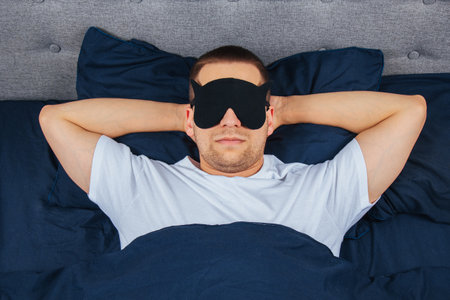 Top view high angle photo of young man wearing sleep mask, happy positive smile, sleep blanket, blanket, clothes, pajamasの写真素材