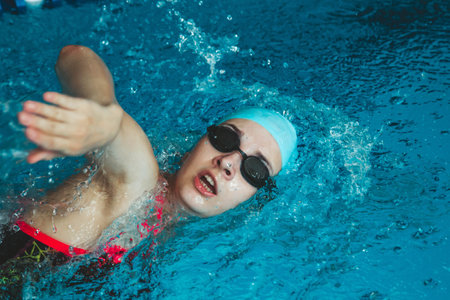 A young swimmer performs a forward crawl technique. The theme of sports and endurance. Side view of a professional female swimmer with goggles at the pool. close-up. A woman swimmer dives into a pool of water. The girl swims underwater in a large poolの写真素材