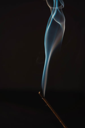 Incense burning smoke fumes and wisps. Aromatherapy smokes for yoga. Aroma sticks smoke on black background with white backlit. Burning aromatic incense smoky stick for meditation and relaxing.の写真素材