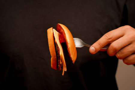 Close up shot of young man eating burger. Home delivery. Man holds burger with hands. Hands holding homemade beef burger on wooden table. Ready to eat tasty fast food hamburger. Unhealthy food concept.の写真素材
