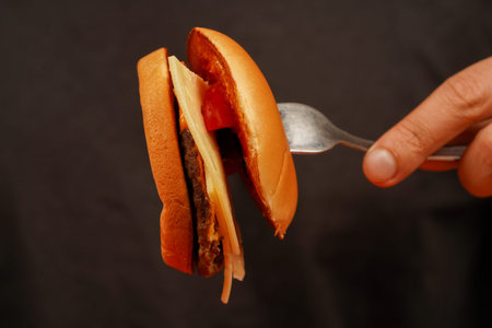 Hands holding homemade beef burger on wooden table. Ready to eat tasty fast food hamburger. Man holds burger with hands. Home delivery. Close up shot of young man eats burger.の写真素材