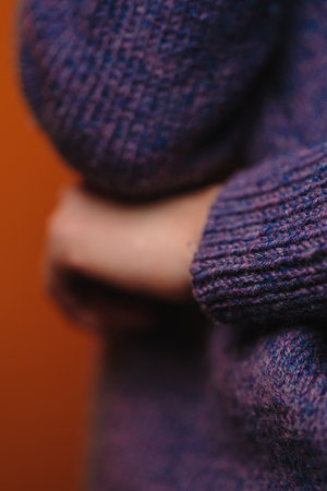 A woman in purple knitted sweater put her hand under elbow, without her face seen, closeup shot. Sign of closeness and uncertainty. Non-verbal sign language, vertical picture.の写真素材